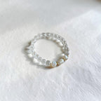 A beaded stretch ring featuring clear faceted crystal beads and three white baroque shell beads, displayed on a textured white surface.