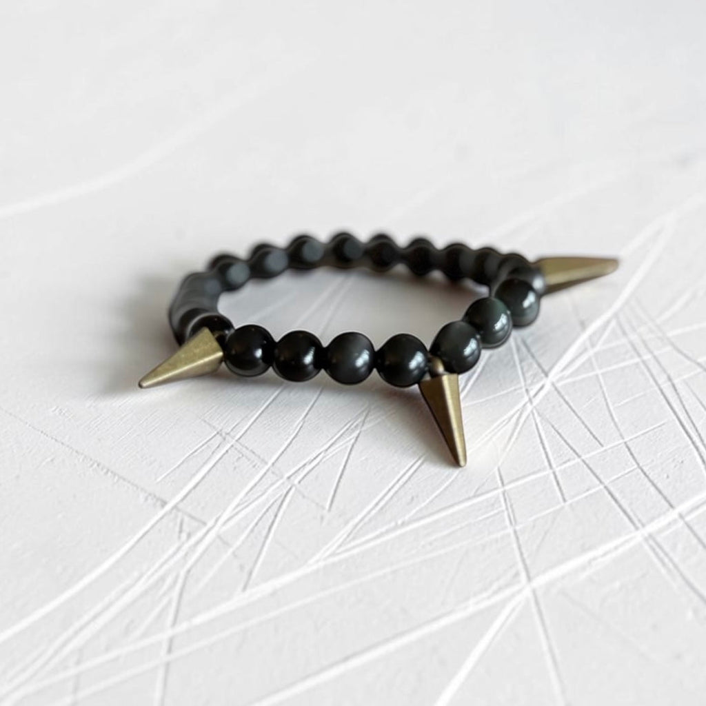 Black bead bracelet with subtle green swirls and brass spikes. Sitting on a white scratch table. 