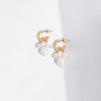 A pair of gold hoop earrings with dangling white baroque pearls, photographed on a clean white background with a soft diagonal shadow.