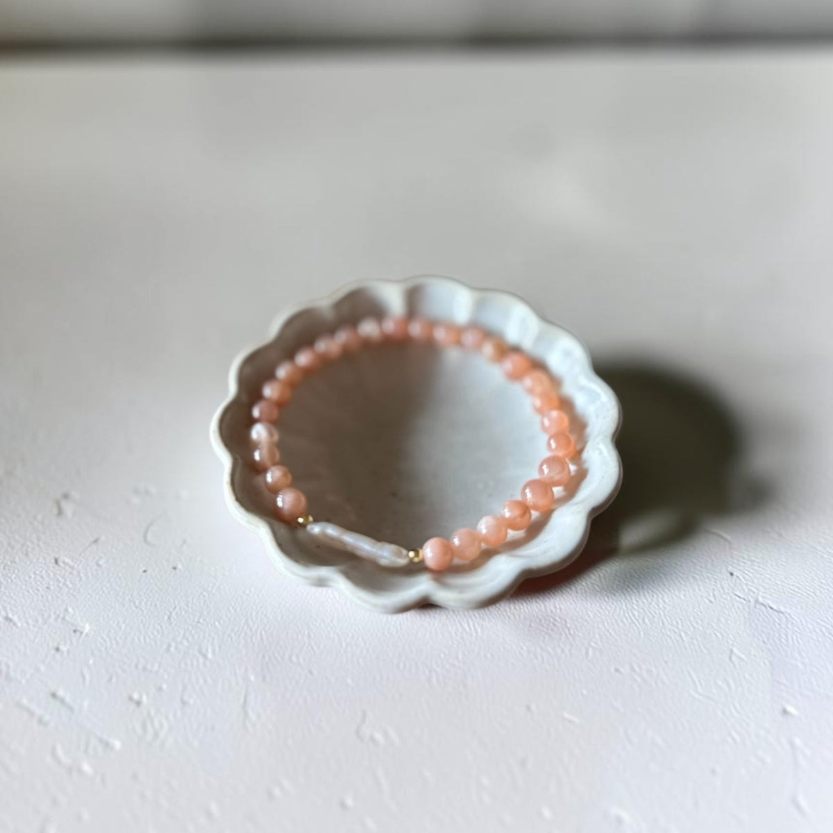 A peach-colored beaded bracelet displayed on a small white ceramic dish against a neutral light gray background.