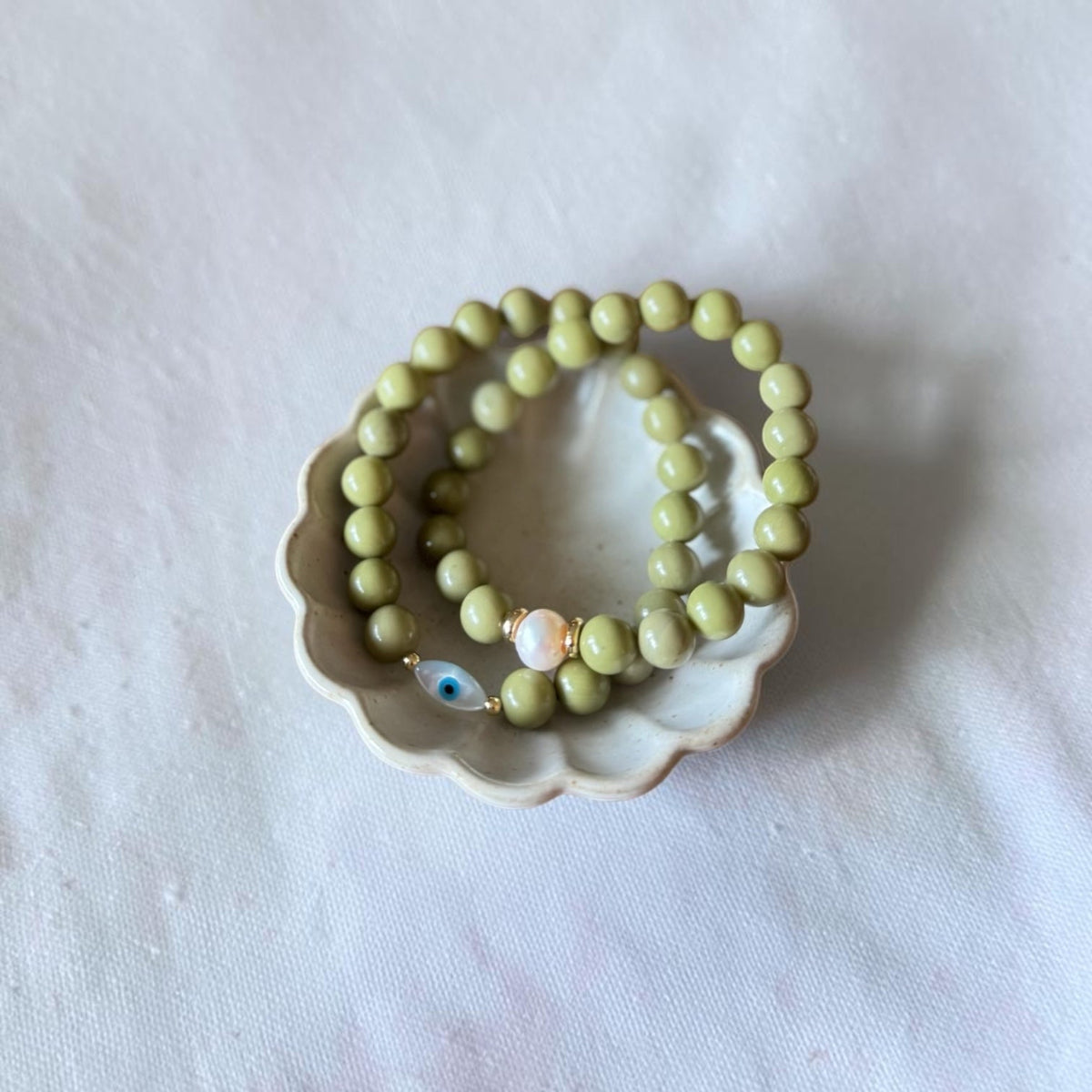 Close-up of The Romy Bracelet showing the mother of pearl evil eye charm and gold filled beads — Poppies & Jules> it also has another green bracelet wth a pearl. 