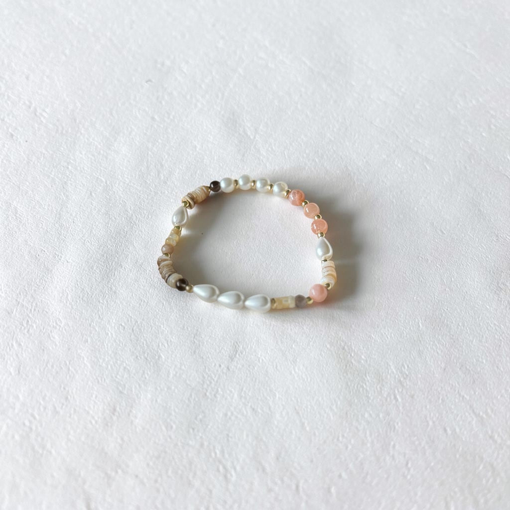 A beaded stretch bracelet featuring white pearls, light pink beads, and natural agate beads, displayed on a textured white surface.