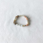 A beaded stretch bracelet featuring white pearls, light pink beads, and natural agate beads, displayed on a textured white surface.