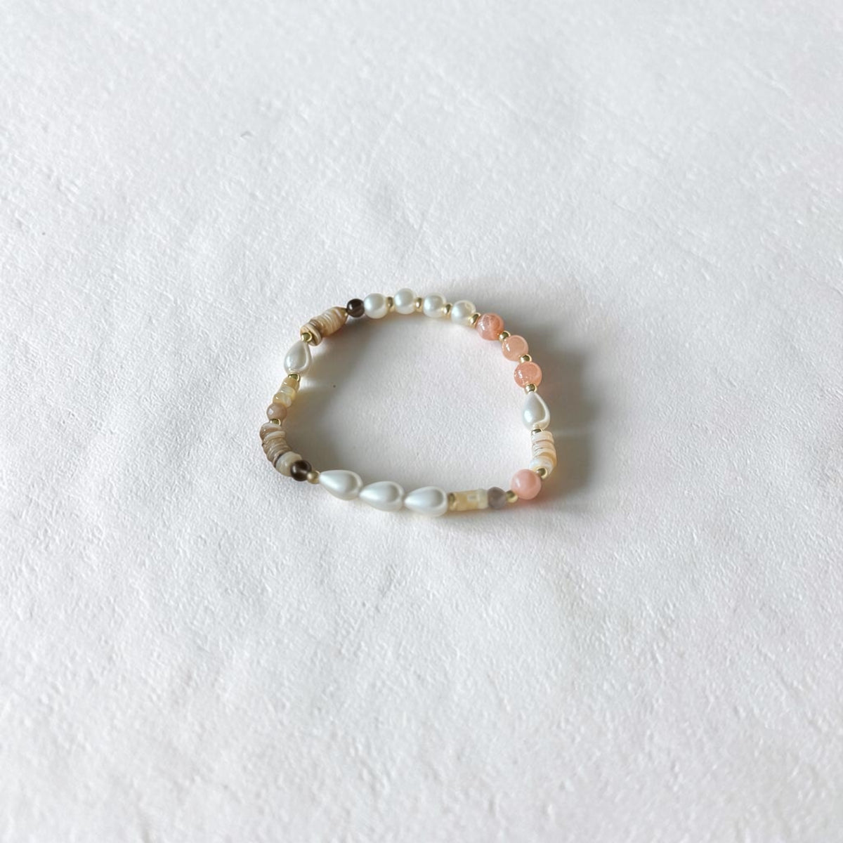 A beaded stretch bracelet featuring white pearls, light pink beads, and natural agate beads, displayed on a textured white surface.