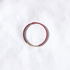 A delicate red beaded bracelet with a small gold chain accent on one side, displayed on a textured white background.