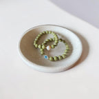 Close-up of The Romy Bracelet showing the mother of pearl evil eye charm and gold filled beads — Poppies & Jules> it also has another green bracelet wth a pearl. 