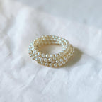 A multi-strand pearl ring with a gold-toned setting, resting on a textured white fabric background.