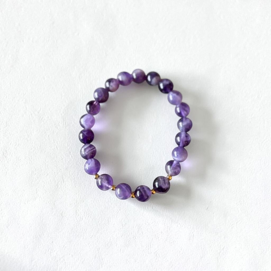 A beaded stretch bracelet made of polished purple gemstone beads with small gold spacer beads, displayed on a clean white background.