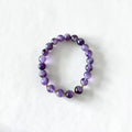 A beaded stretch bracelet made of polished purple gemstone beads with small gold spacer beads, displayed on a clean white background.