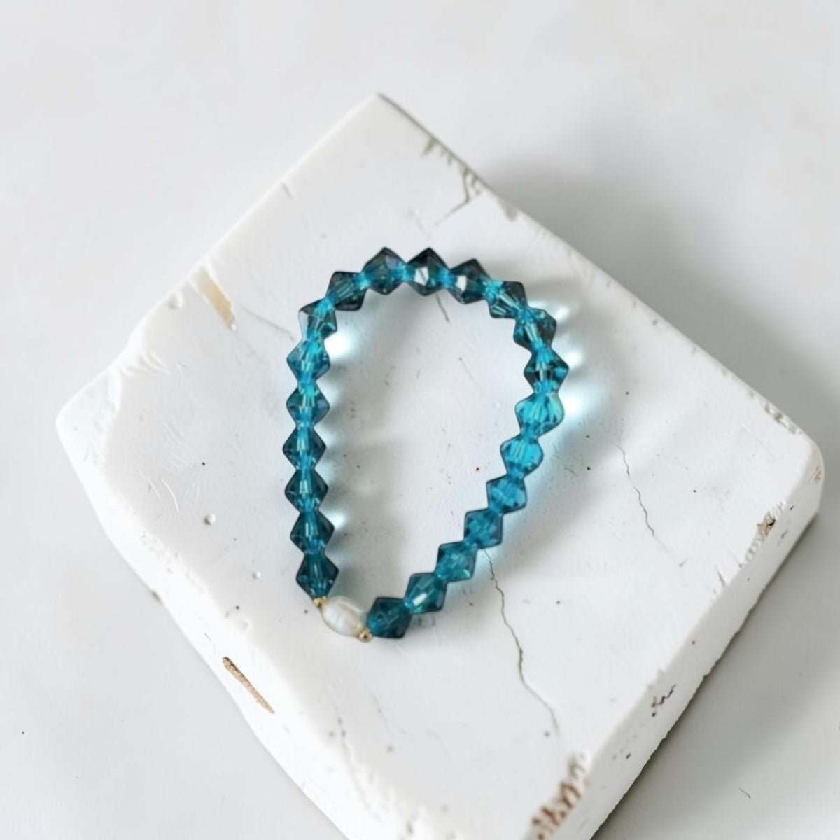 A beaded stretch bracelet made of faceted blue beads, displayed on a white textured stone tile against a light background.