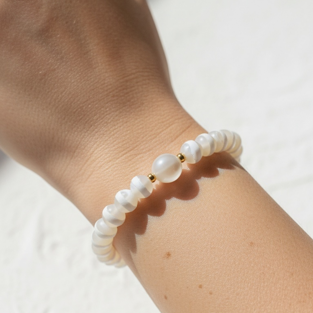 A close-up of a beaded bracelet worn on a person's wrist. The bracelet features matte white round beads with a central larger white bead, accented by small gold spacer beads.