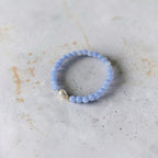 A light blue 6mm stack bracelet with a teardrop pearl and gold filled beads surrounding it. This bracelet is sitting on cement. 