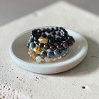 A group of 10mm bead bracelets sitting it a cement like bowl. Varies in neutral colors from light to dark.