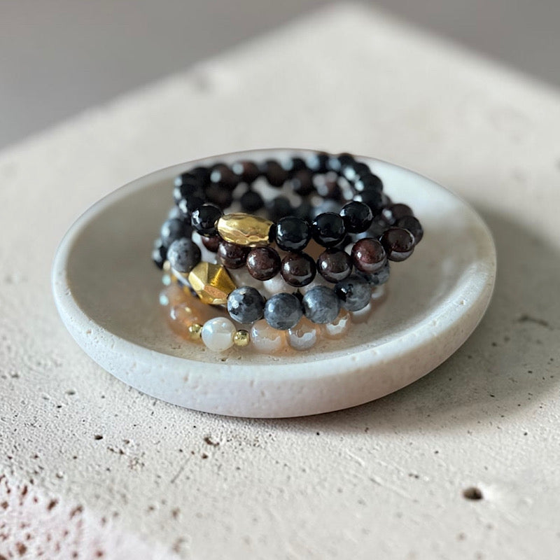 A group of 10mm bead bracelets sitting it a cement like bowl. Varies in neutral colors from light to dark.