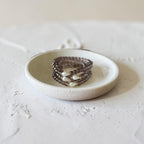 A stack of three beaded wrap bracelets in a dark brown smoky color with small white pearl-like beads, displayed on a small round ceramic dish.