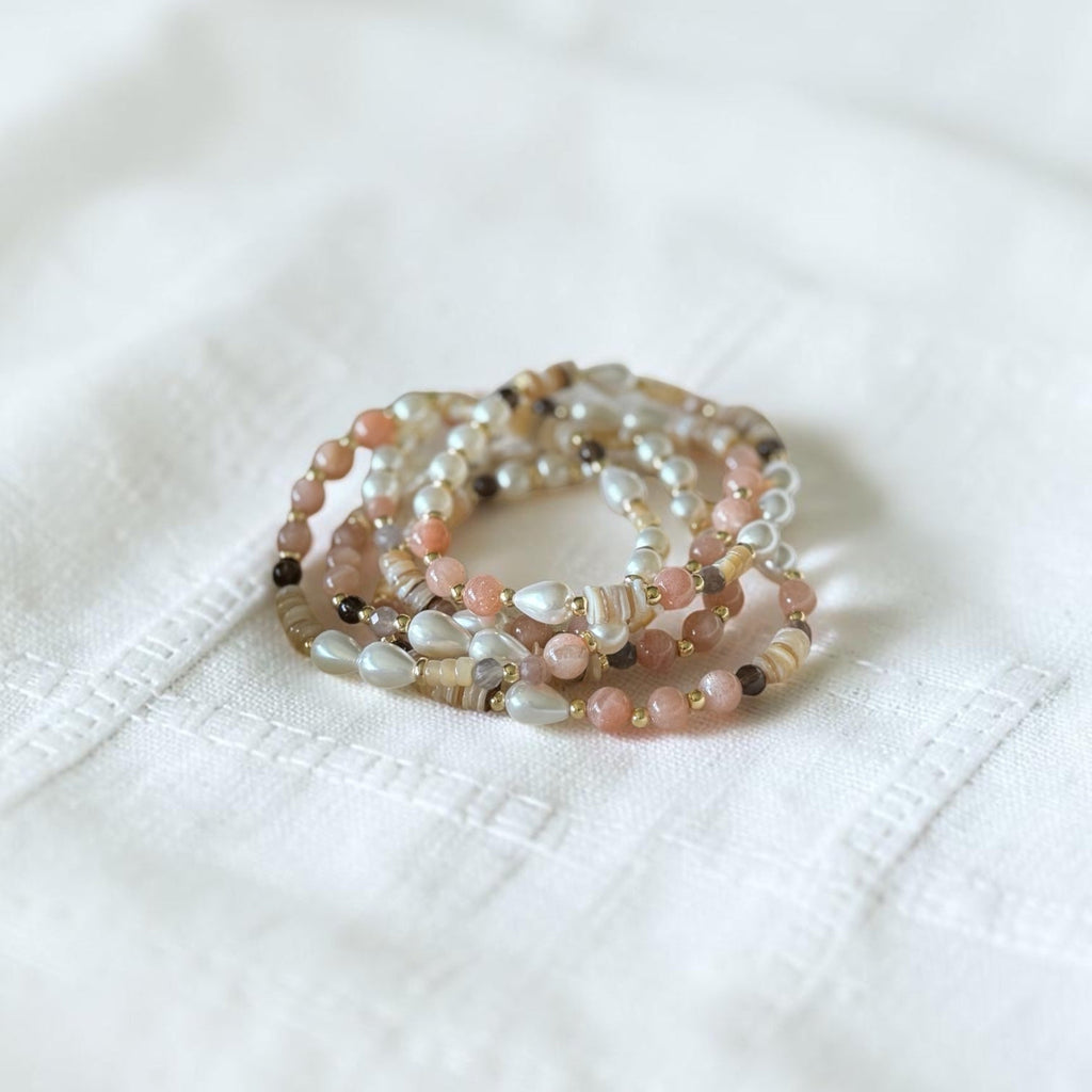 A stack of multi-strand beaded bracelets resting on a textured white fabric background.