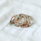 A stack of multi-strand beaded bracelets resting on a textured white fabric background.
