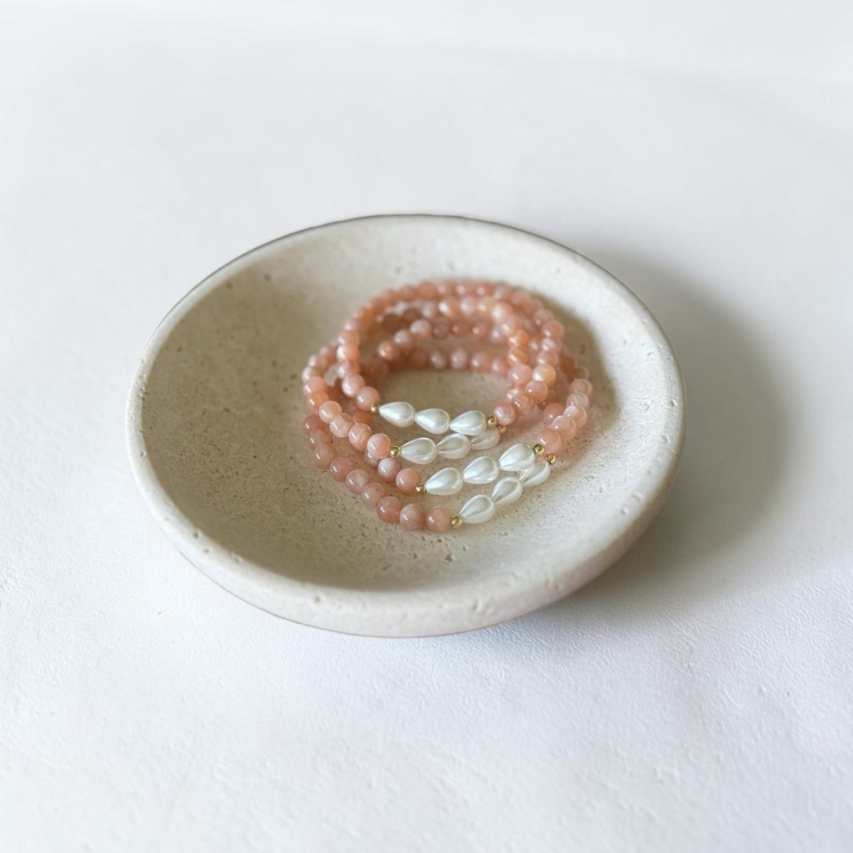 A set of three beaded bracelets in dusty pink and white, displayed on a small speckled ceramic dish against a clean white background.