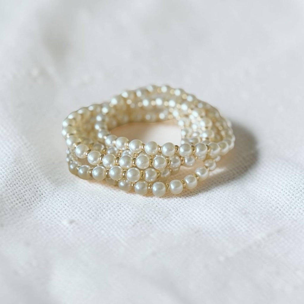 A pearl bracelet with gold-toned metal settings, resting on a textured white fabric background.