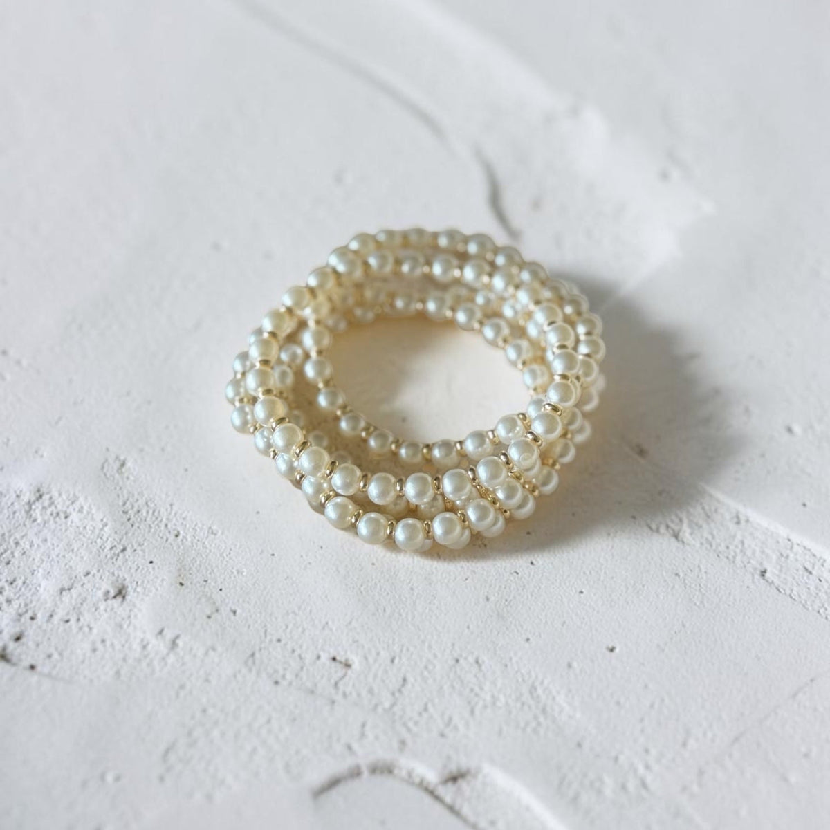 Pearl bracelets stack photographed on a textured white surface.