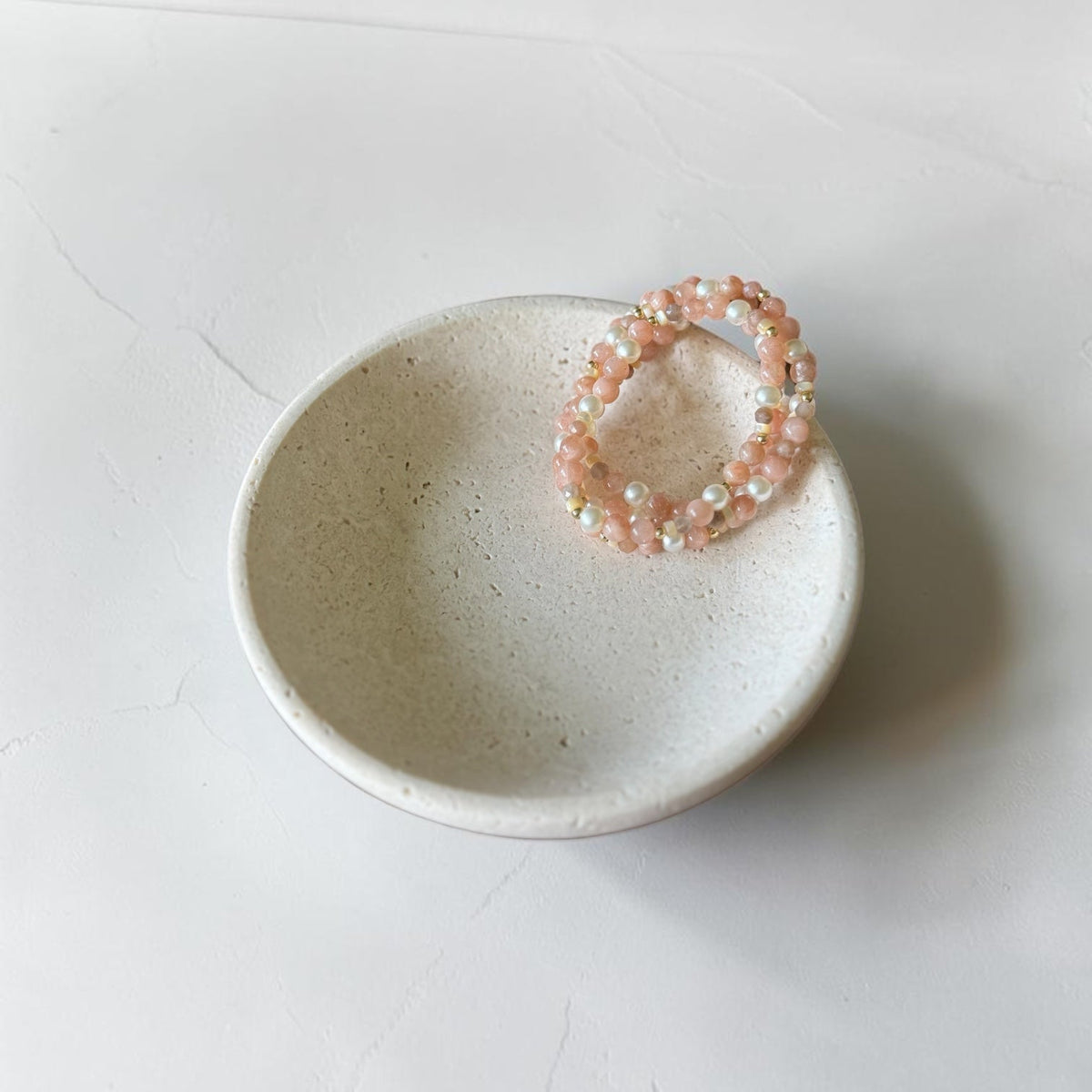 A peach and white beaded stretch bracelet displayed on a small speckled ceramic dish against a light gray background.