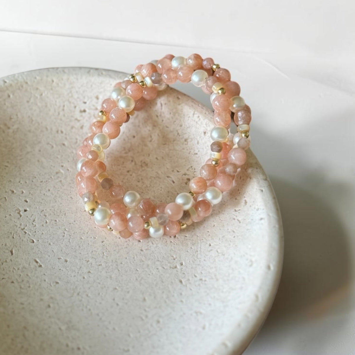 A double-strand beaded stretch bracelet with pink stone beads and white pearl-like beads, displayed on a small speckled ceramic dish.