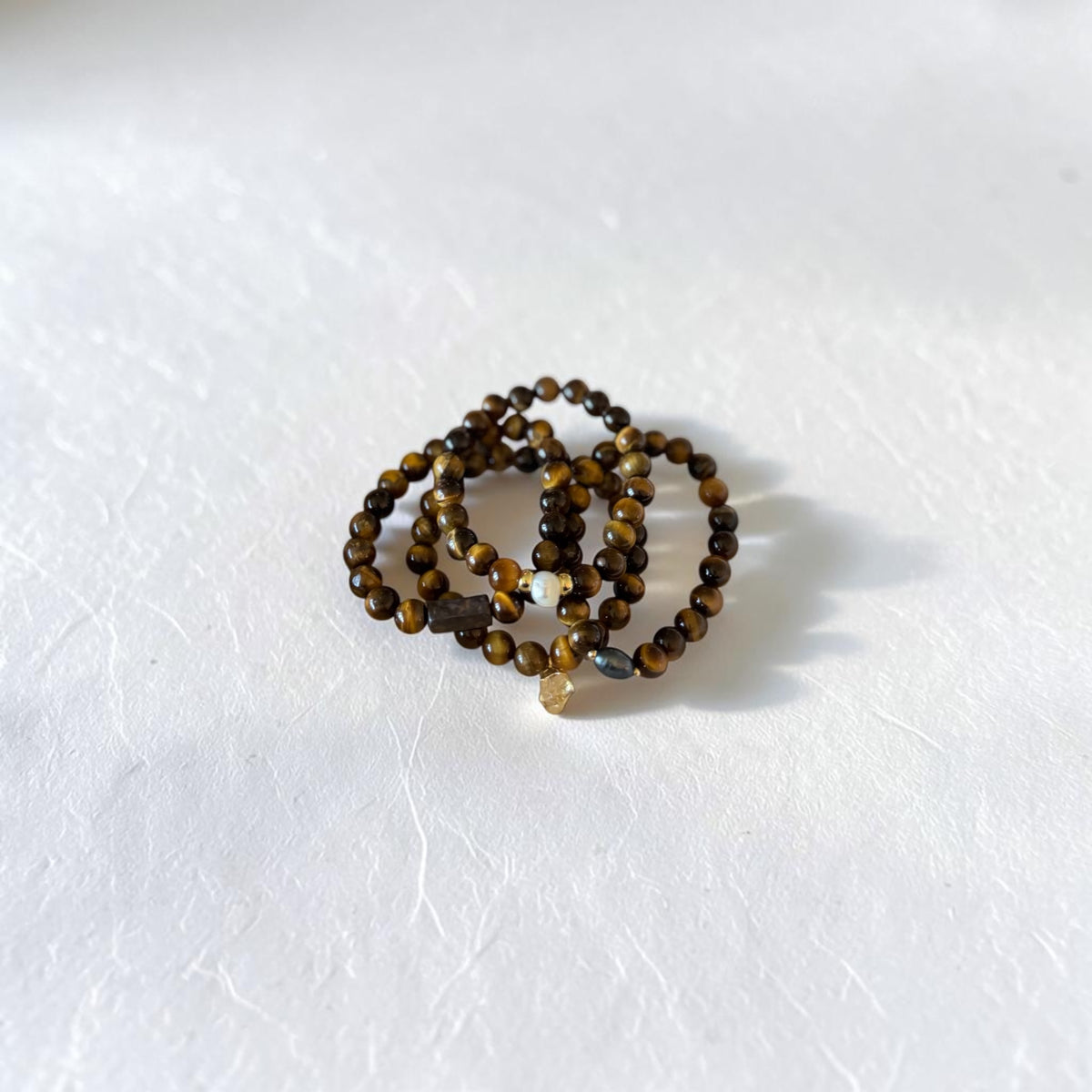 A set of beaded stretch bracelets in shades of brown, black, and gold, arranged in a small coil on a textured white surface.