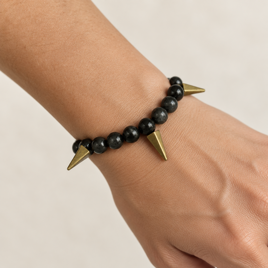Bracelet on a wrist. Beads are black with swirls with brass spikes. 