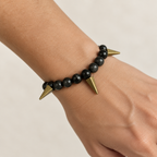 Bracelet on a wrist. Beads are black with swirls with brass spikes. 