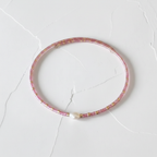 The Bloom Bracelet - flat lay. Close up of a seed bead pink wire bracelet with a fresh water pearl nugget in the middle.