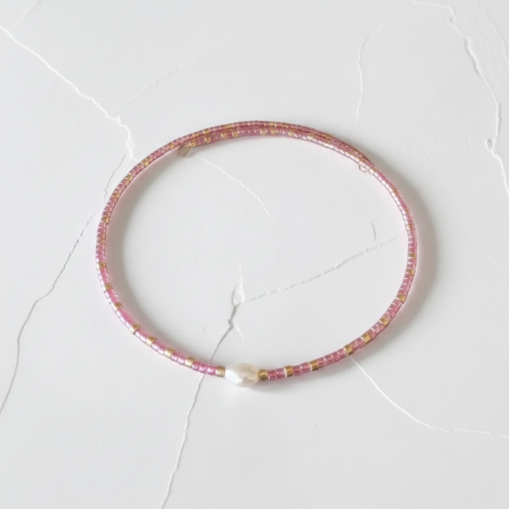 The Bloom Bracelet - flat lay. Close up of a seed bead pink wire bracelet with a fresh water pearl nugget in the middle.