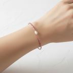 The Bloom Bracelet - smaller pearl wrist shot. This is a thin wire seed bead bracelet in pink with a cute little pearl in the middle. It is siting on an arm.