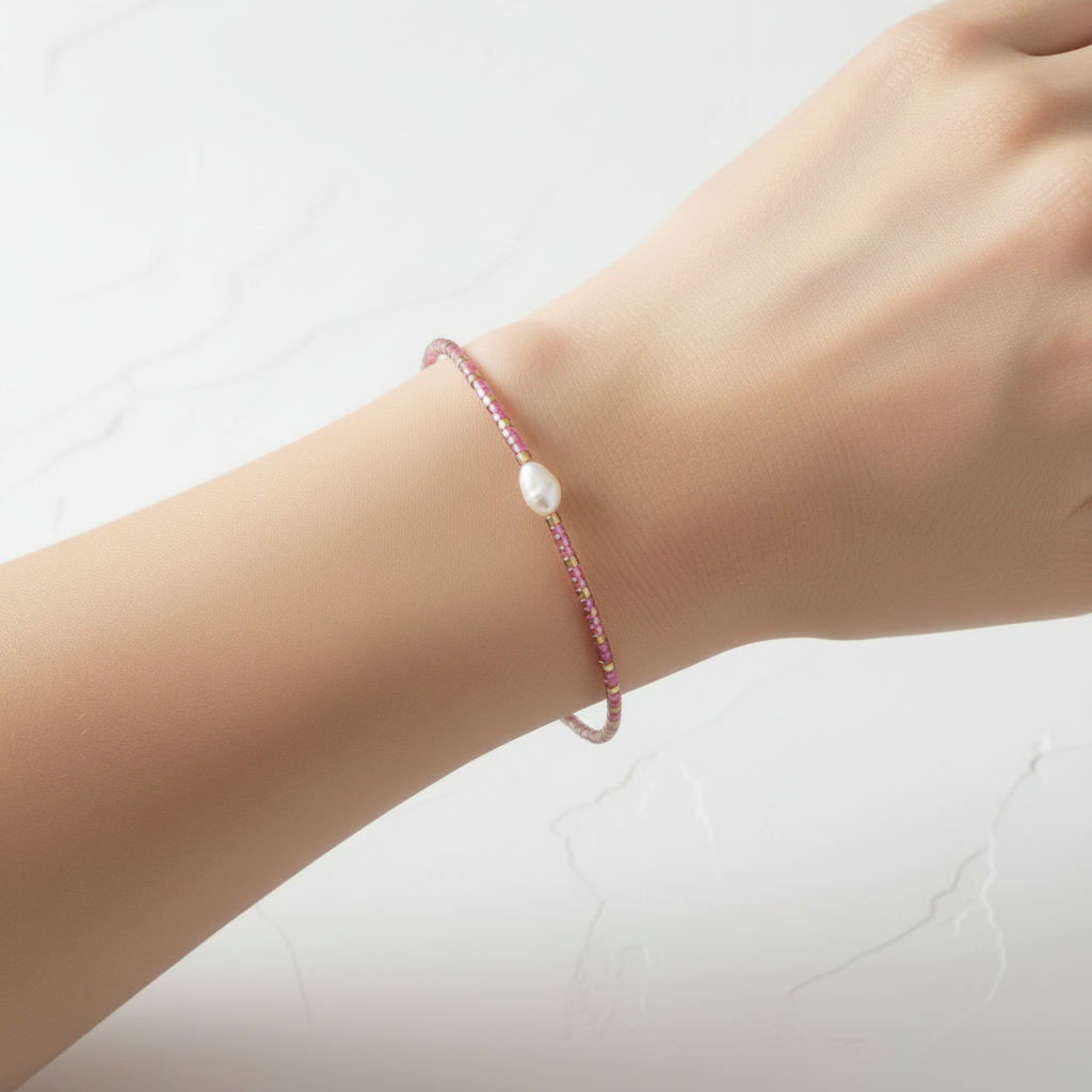 The Bloom Bracelet - smaller pearl wrist shot. This is a thin wire seed bead bracelet in pink with a cute little pearl in the middle. It is siting on an arm.