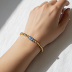 The Caspian Bracelet wrist shot of small gold filled beads with a longer blue accent bead in front. This is sitting on an arm.