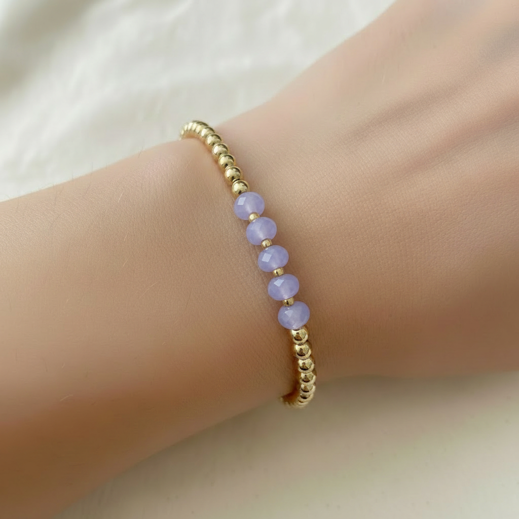 The Colette Bracelet on wrist. This is a clsoe up of an arm that shows the gold filled beads with purple beads in front.