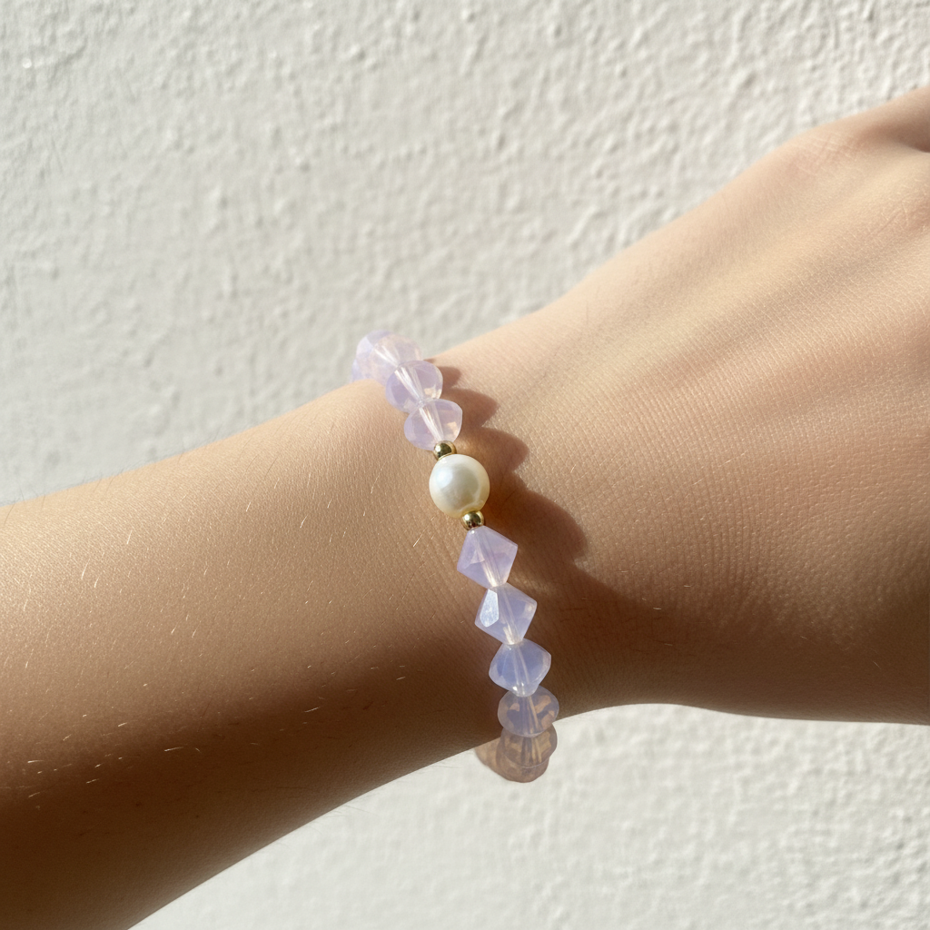 The Elena Bracelet Wrist Shot. Background is white texture, close up is an unique shape purple beads with a fresh water pearl. Gld beads surround the pearl.