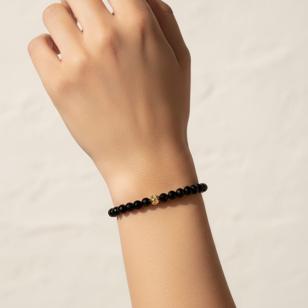 The Ella Bracelet is a clsoe up of a female arm and wrist. There is 6mm black beads with a gold fileld nugget in front.