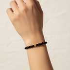 The Ella Bracelet is a clsoe up of a female arm and wrist. There is 6mm black beads with a gold fileld nugget in front.