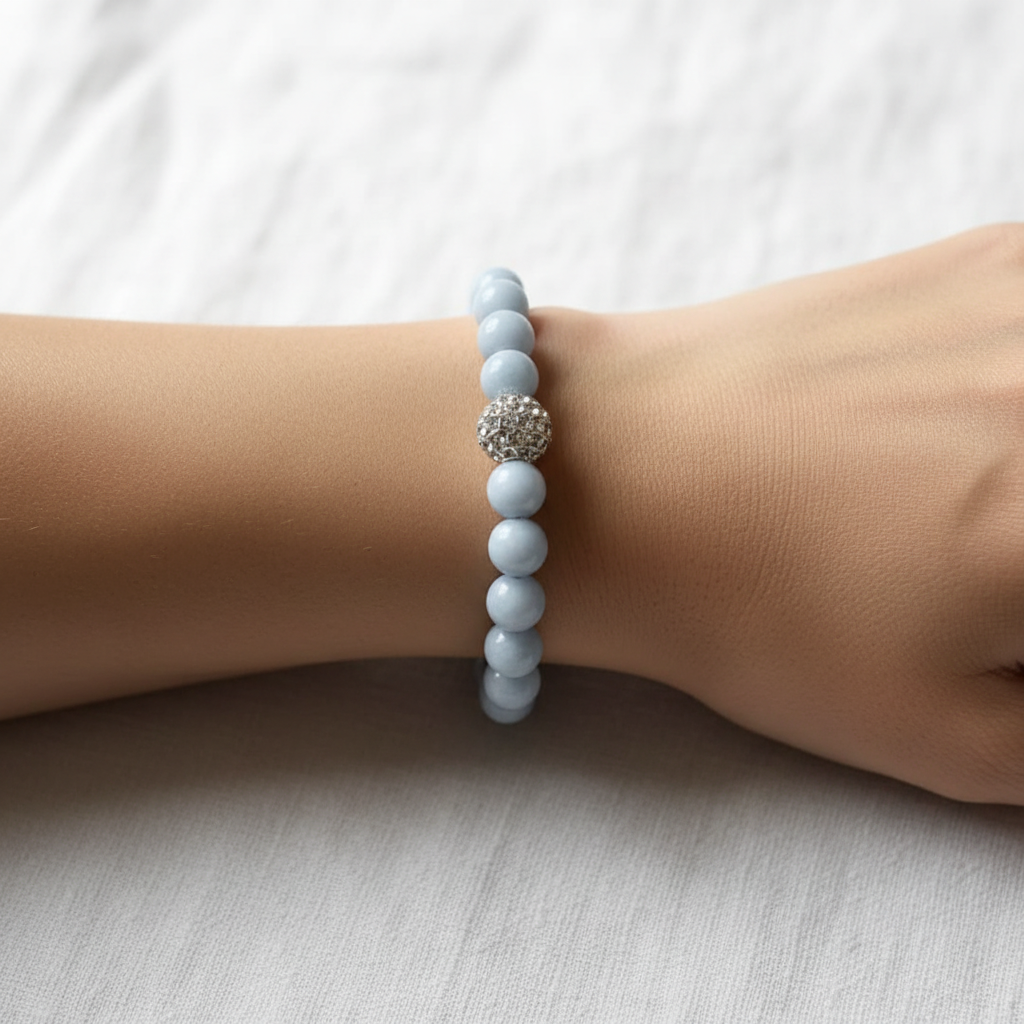 The Eve Bracelet wrist shot. There is an arm sitting on white fabric. The bracelet is a beautiful blue with a rhinestone silver accent bead front in center.