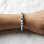 The Eve Bracelet wrist shot. There is an arm sitting on white fabric. The bracelet is a beautiful blue with a rhinestone silver accent bead front in center.