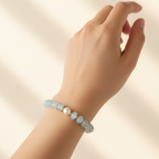 The Fallon Bracelet. This is a picture of a clsoe up female wrist/arm. On the wrist is light blue rondelle beads surrounded by gold filled beads. There is a fresh water pearl front and center.
