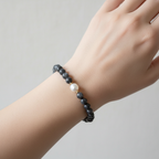 The Greer Bracelet. This is a clsoe up of a female wrist. There are dark beads with a pearl in the front. Gold spacers surrounding the pearl. 
