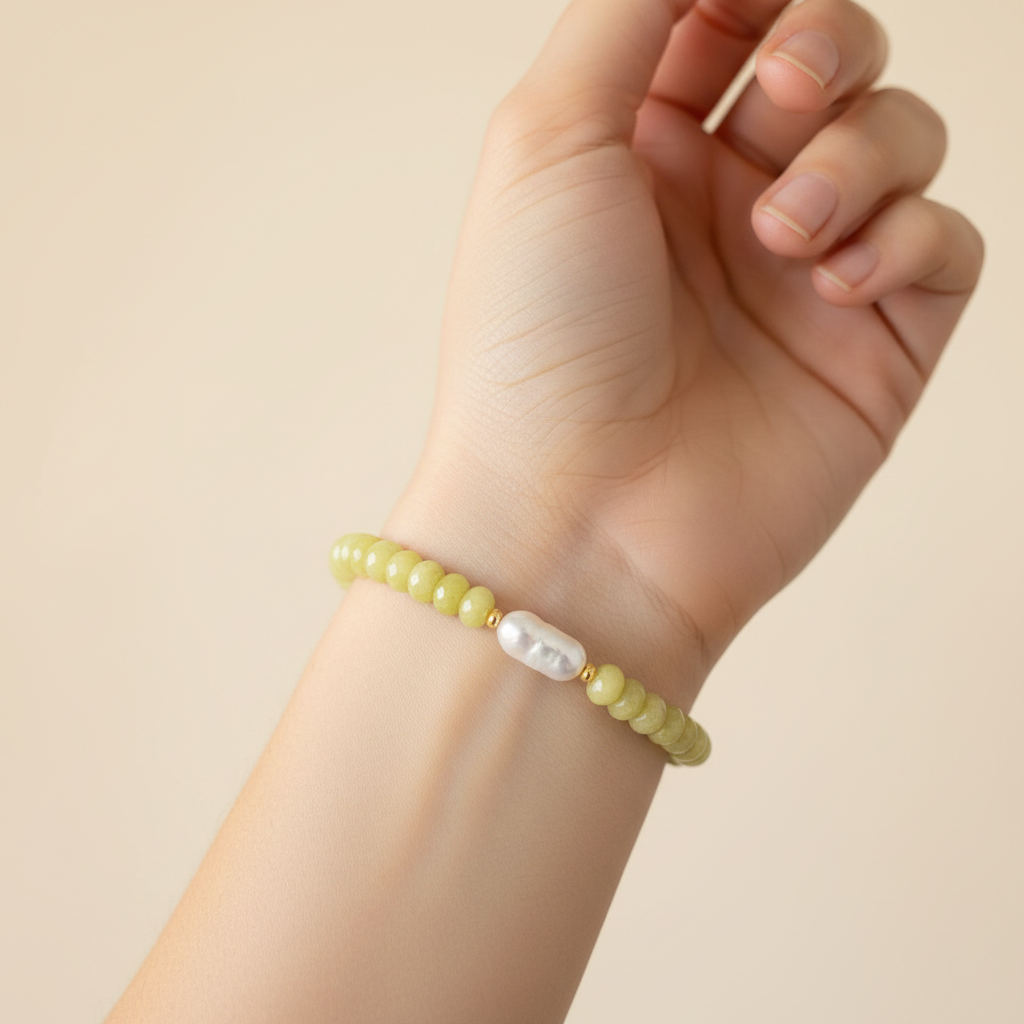 The Junelle Bracelet is a close up of a female wrist. On the wrist is greenish yellow rondelle beads with a rectangle pearl. Gold plated spacers surrond the pearl.