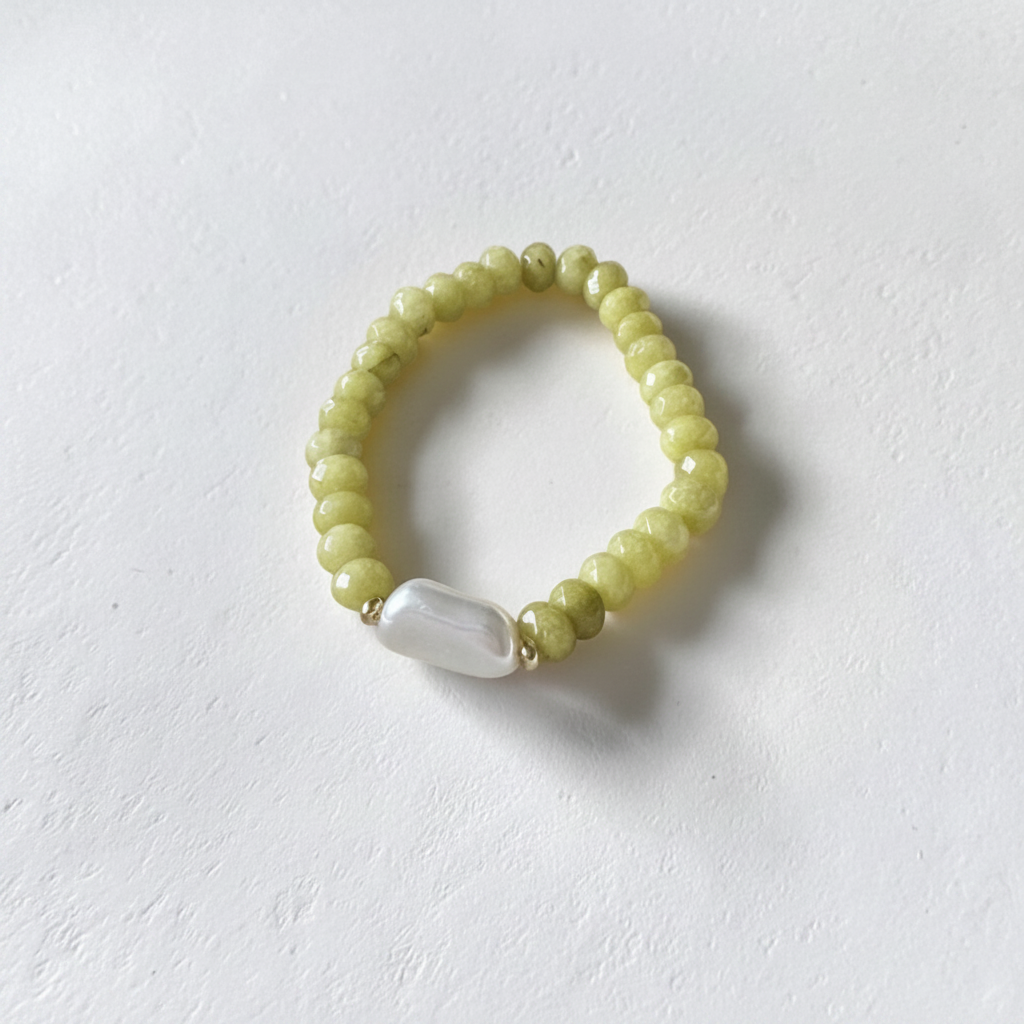 The Junelle Bracelet is sitting on white background. Close up of rondelle green beads with a long rectangle pearl. Gold plated spacers surrounding the pearl.