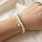 The Lani Bracelet on wrist. Arm is sitting on the ivory fabirc. The bracelet is a gorgeous moonstone white bead with a shell charm in the center.