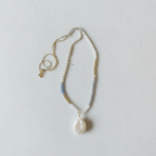 The Malia Necklace - white background. Necklace sits on slightly texture background.