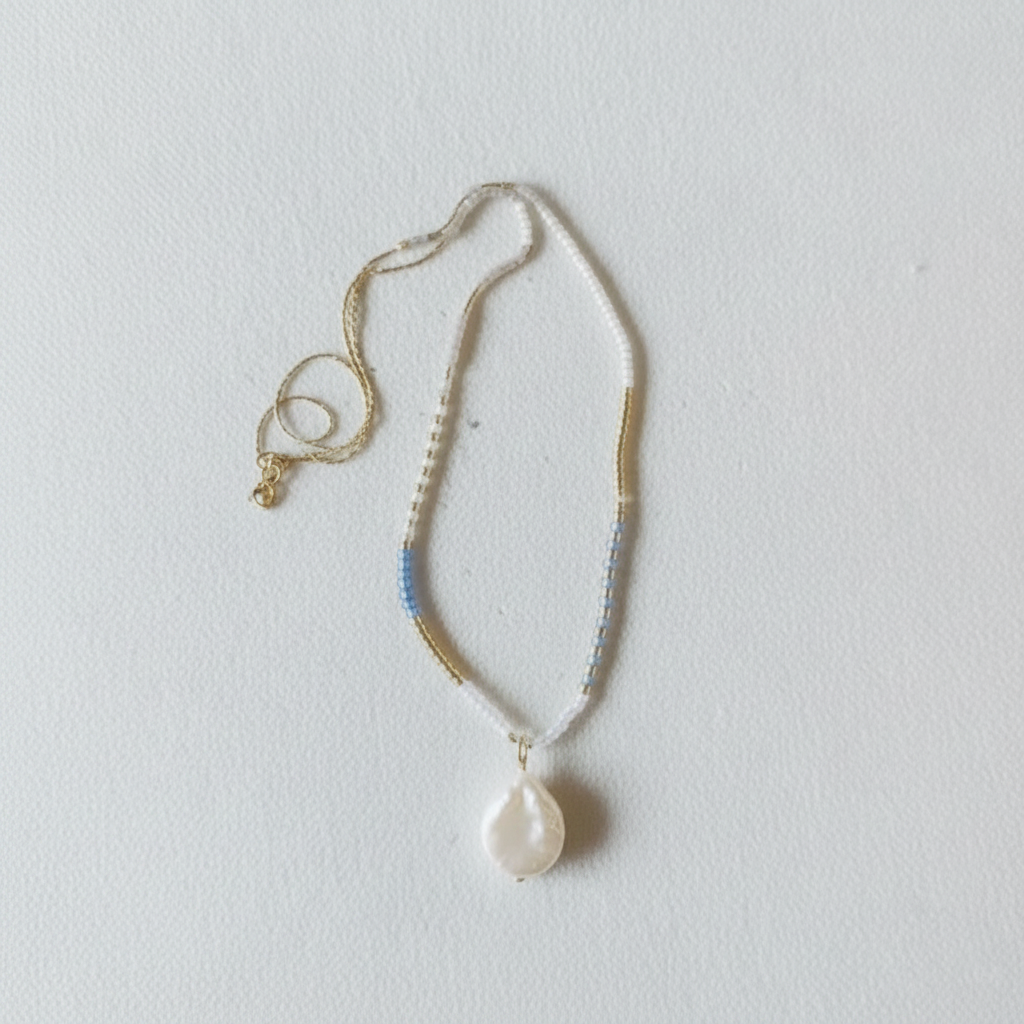 The Malia Necklace - white background. Necklace sits on slightly texture background.