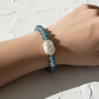 The Marlow Bracelet Wrist Shot. Arm is sitting on white texture table. Bracelet is on the wrist. It is a tie dye like beads with a large fresh water pearl. Gold surround the pearl. 