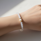 The Monroe Bracelet on Wrist shot. It is a translucent  clearish white bead with a pearl in the front. It is surrounded by gold spacers.