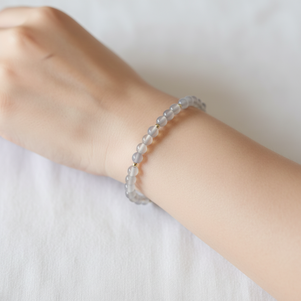 The Pica Bracelet on Wrist. This is a see through gray color with gold fileld beads throughout. The picture is a clsoe up of an arm on white background.